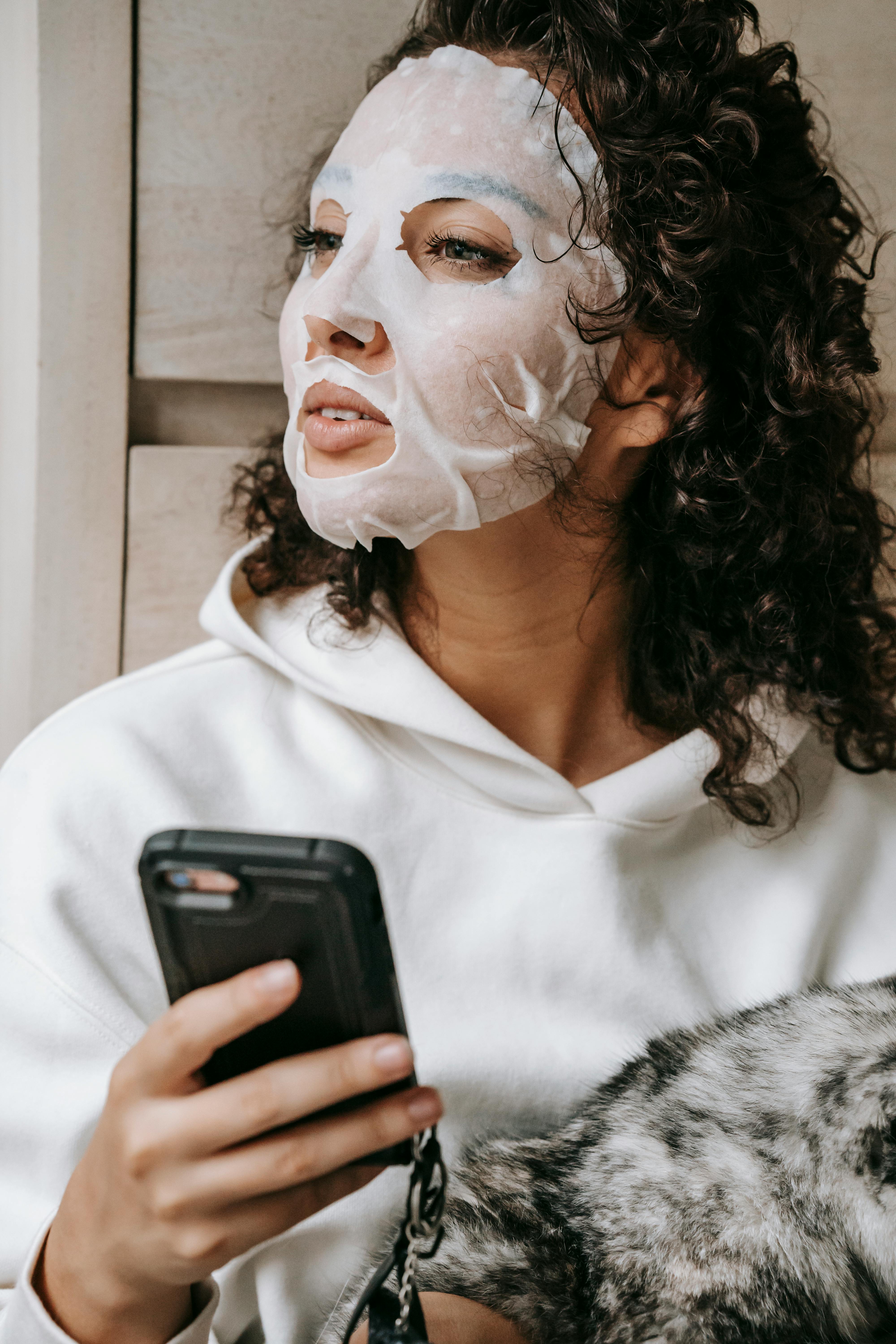dreamy woman in facial mask browsing smartphone