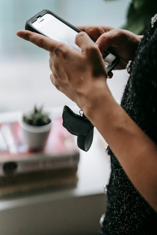 Side view of crop anonymous female text messaging while touching screen on cellphone in house