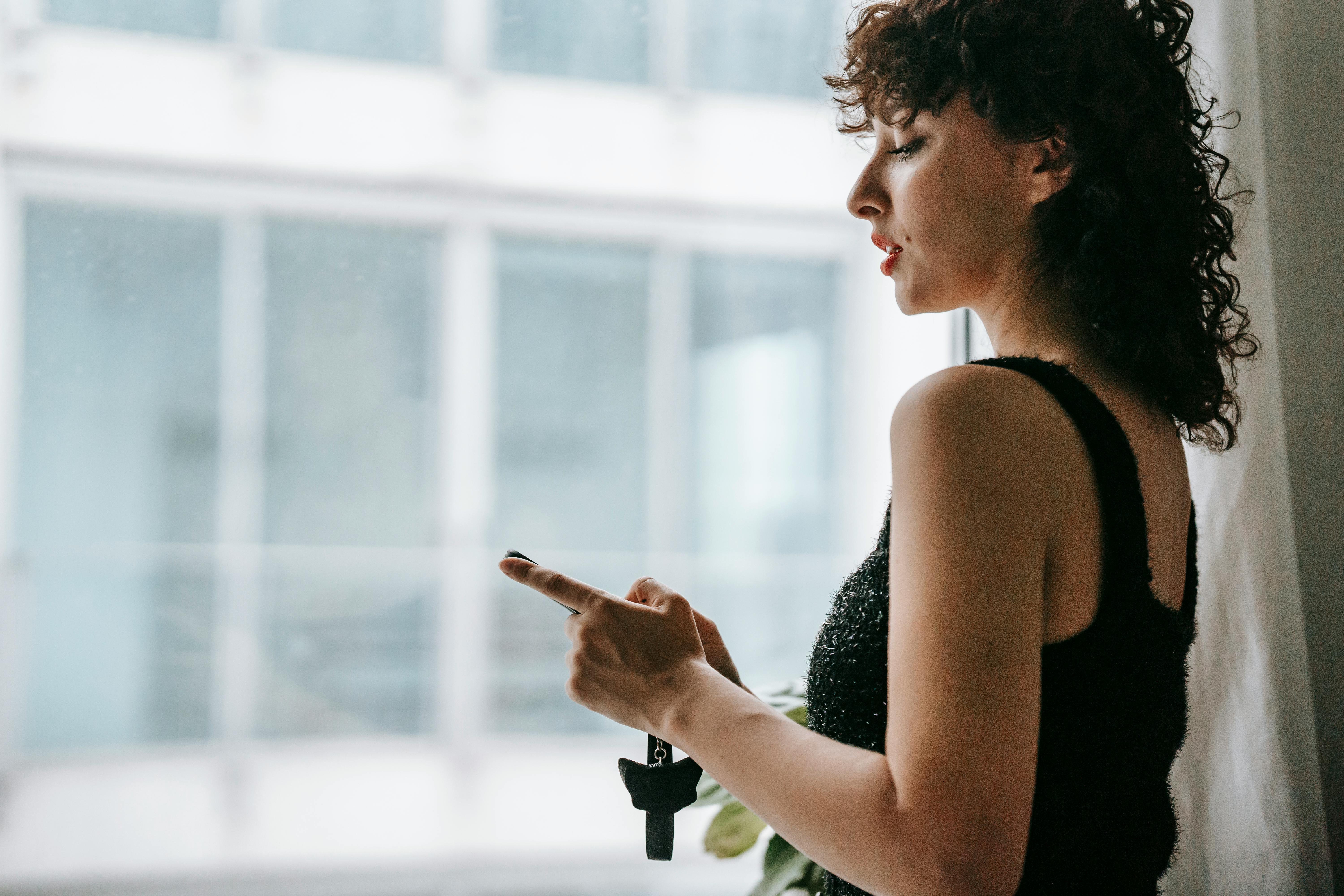 crop attentive woman watching smartphone near window at home