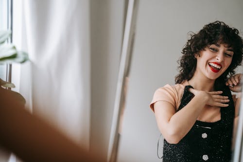 Crop happy woman trying on clothes while looking in mirror