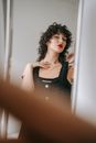 Crop adult female with makeup touching neck while standing with black apparel in front of mirror in house