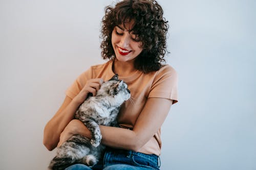 Crop candid female in casual wear caressing and embracing adorable cat on white background