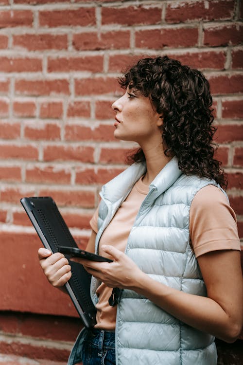 Attentive female remote worker with laptop and smartphone on street