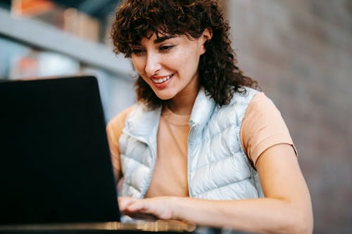 Crop smiling freelancer working on laptop at cafe table outdoors