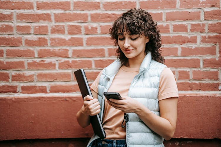 Smiling Freelancer With Laptop Chatting On Smartphone On Street