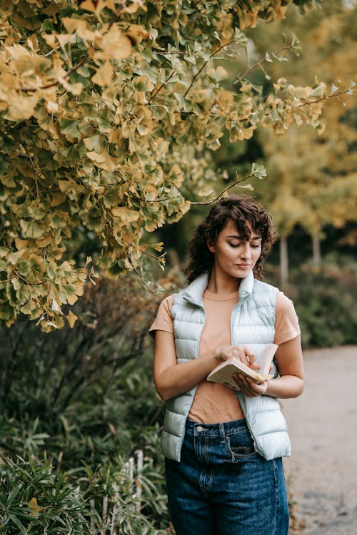 Thoughtful female standing near tree and reading book