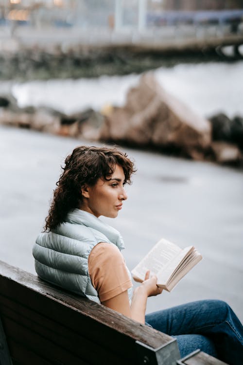 Free Calm female sitting on bench on street and reading book Stock Photo