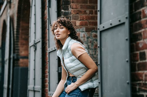 Wanita Berkemeja Putih Dan Jeans Denim Biru Berdiri Di Samping Dinding Coklat