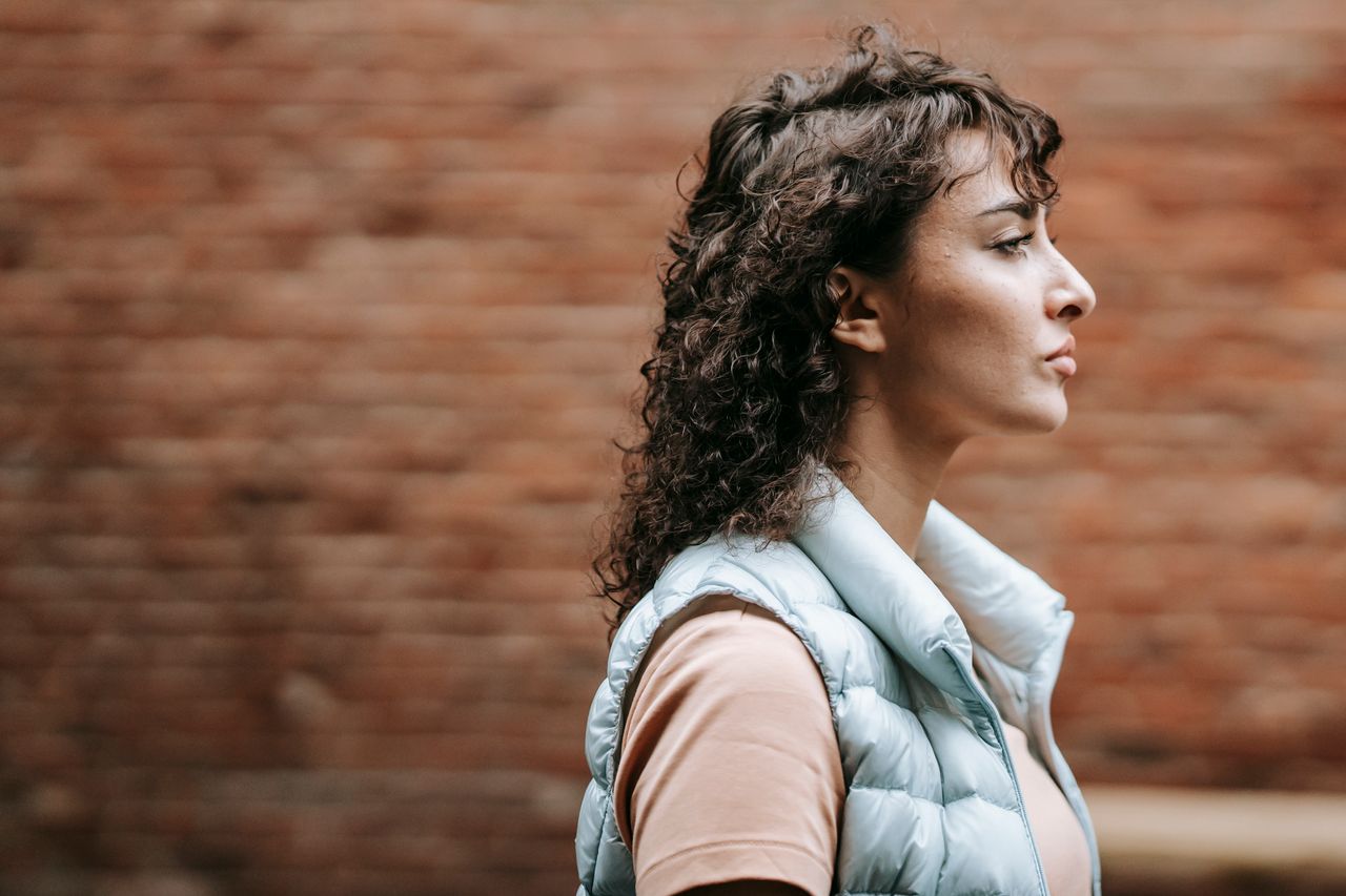 side view of brown haired female in casual clothes standing on city st