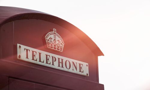 Free Photograph of a traditional red British telephone booth with a crown emblem and sunlight. Stock Photo