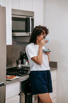 Calm young female in casual outfit with patch on nose drinking coffee while having breakfast in kitchen at home