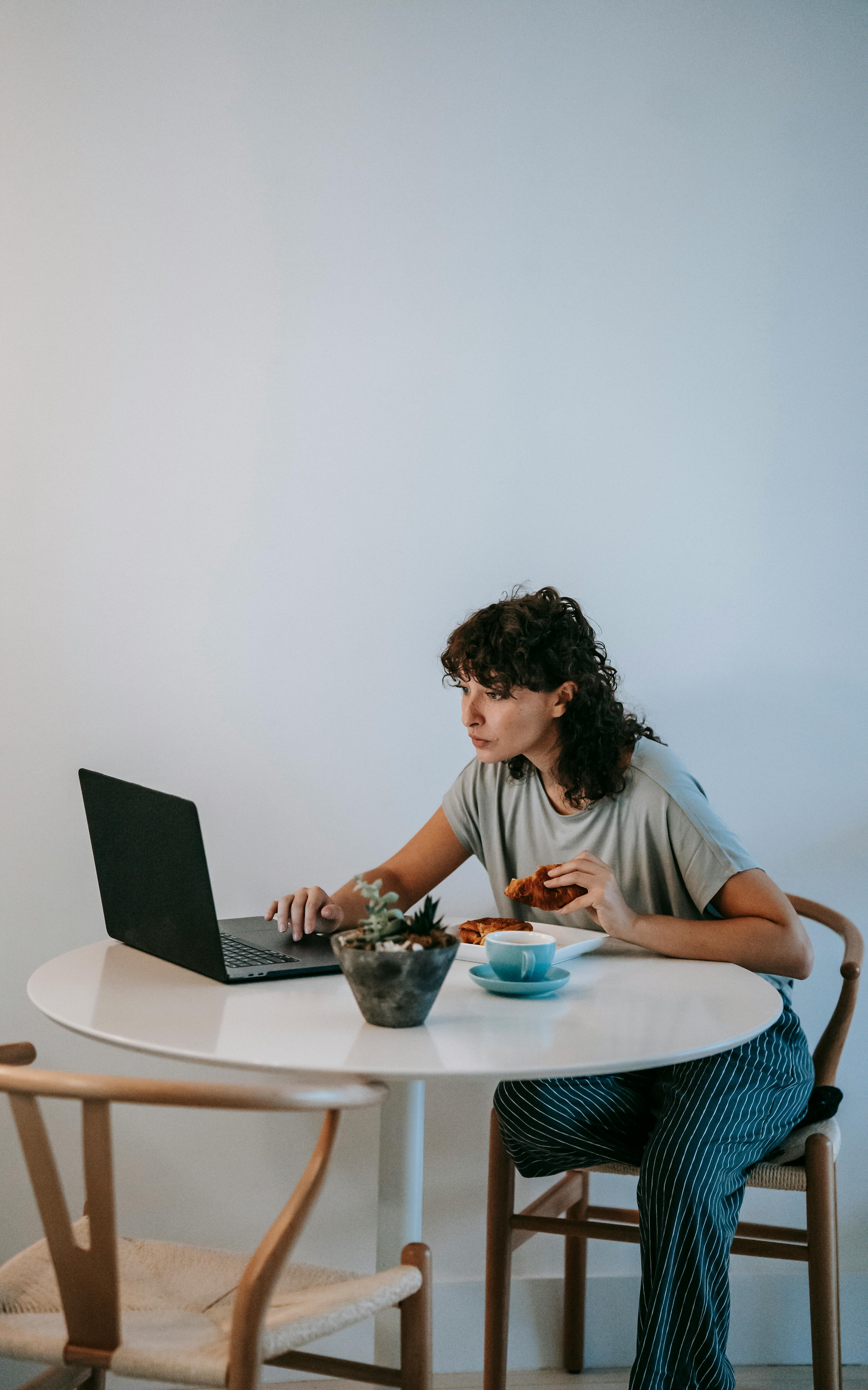 focused woman browsing laptop at table with snacks