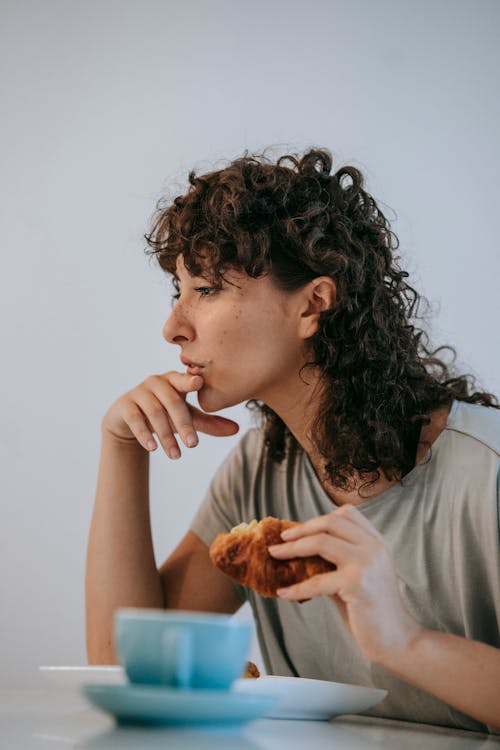 灰色衬衫吃面包的女人