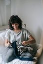 Full body of positive female owner with dappled cat sitting on bed with knitting needles and blue thread in bedroom