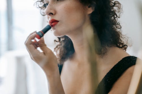 Content young woman applying red lipstick on lips