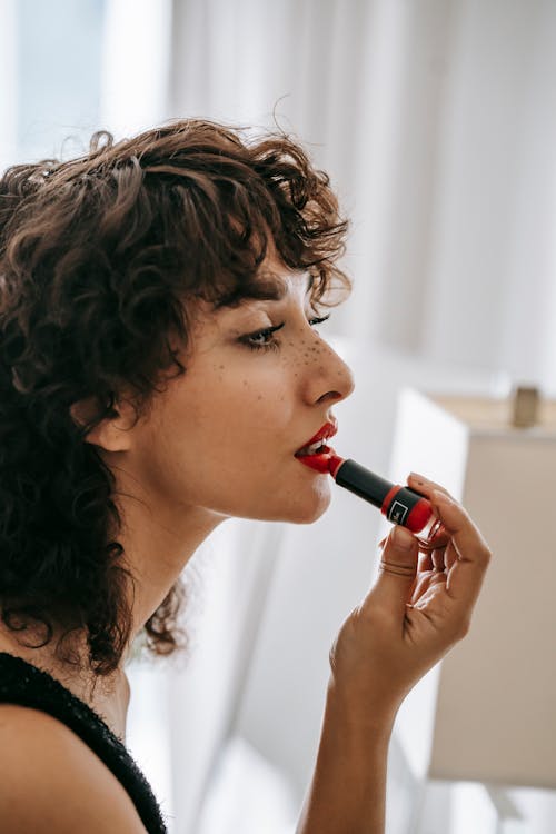 Young content woman applying red lipstick