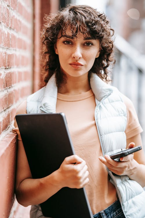 黒のタブレットコンピューターを保持している白い長袖シャツの女性