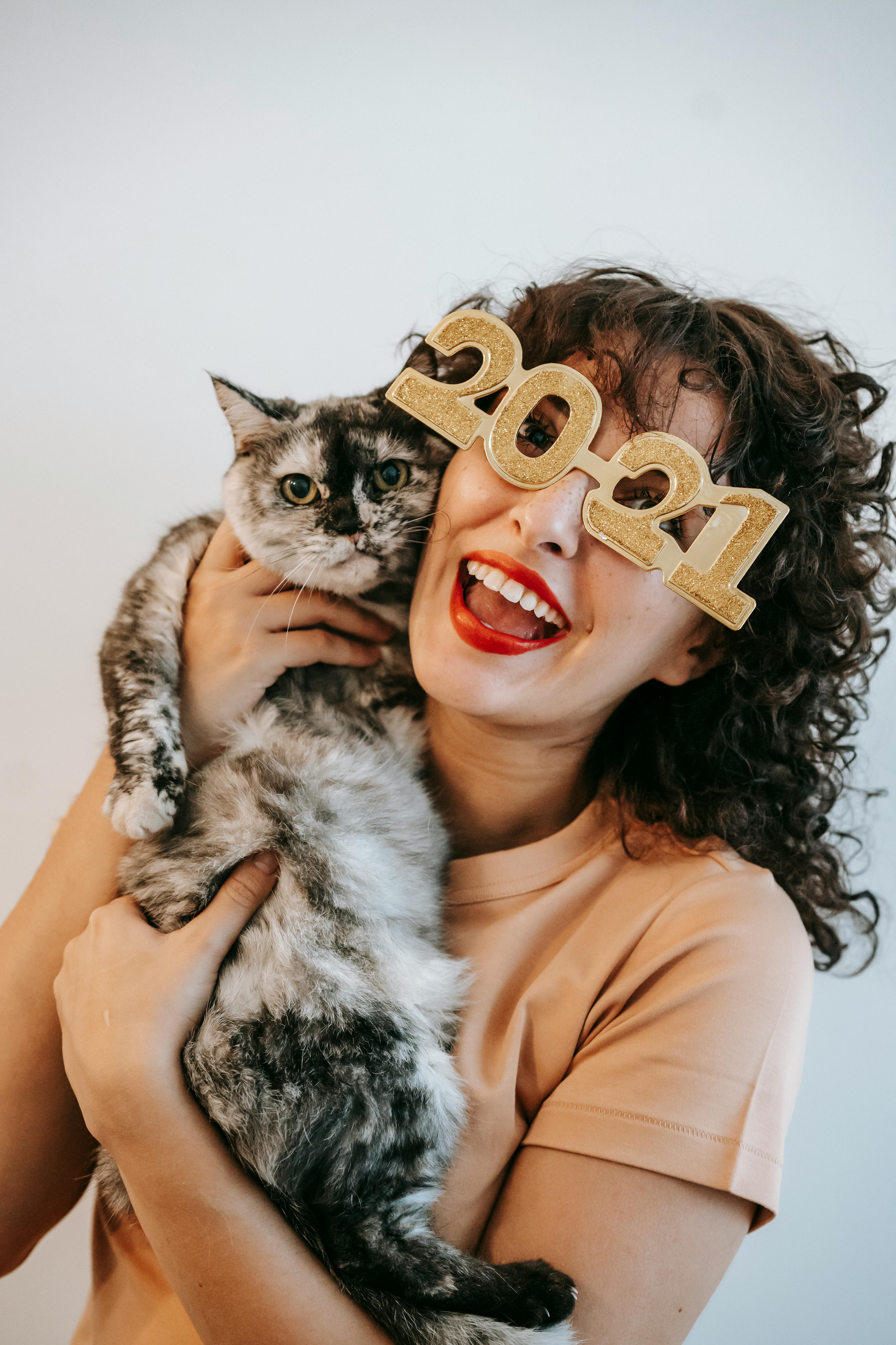 cheerful young woman in decorative new year eyeglasses embracing cat