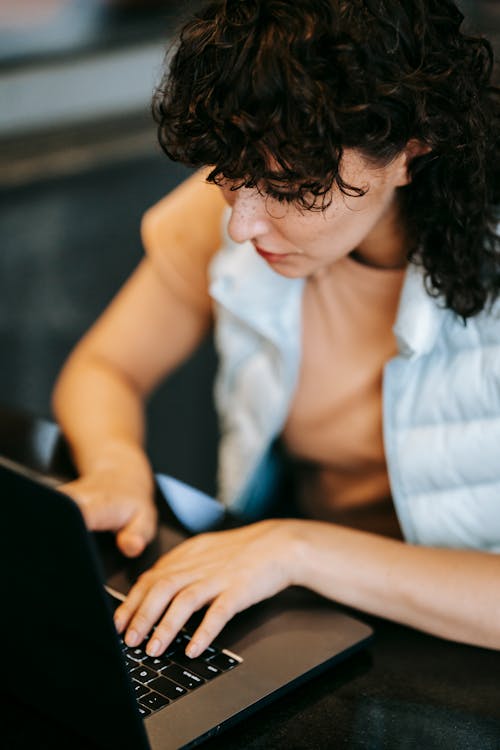 From above of crop young concentrated female using netbook while browsing internet at table