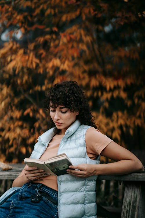 Young woman with dark curly hair reading book in park