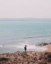 High angle back view of anonymous male backpacker shooting picturesque scenery of wavy sea while standing on sandy shore