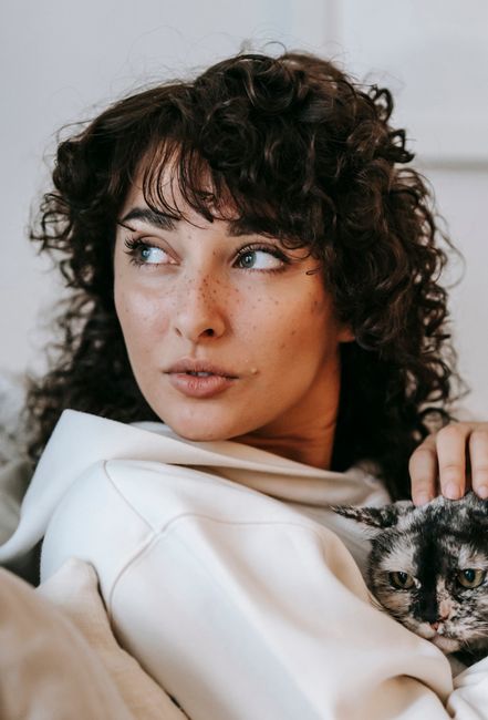 Content young female with dark curly hair stroking fluffy cute spotty cat and looking away