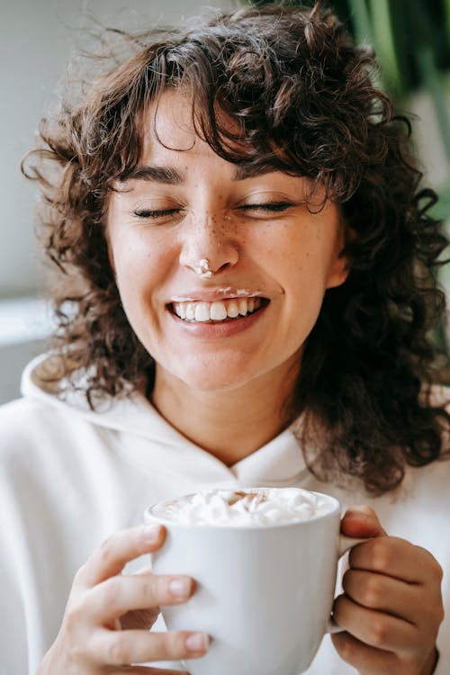 Cheerful woman with cream on nose and cup of coffee