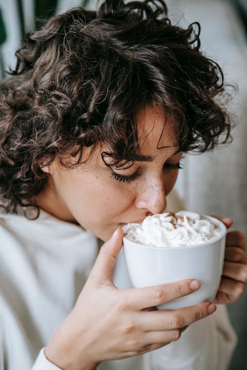 Charming female drinking hot coffee with whipped cream