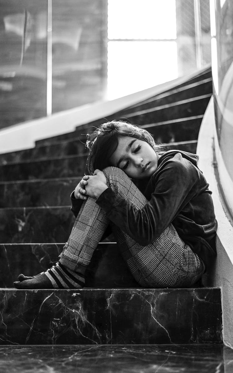 Child Sitting On Stairs With Knees Up To Chin 