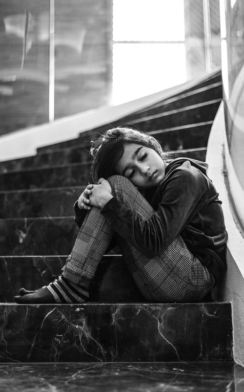 Free Black and white photo of a child sitting on stairs, appearing lonely and upset. Stock Photo