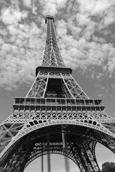 Monochrome photograph of the Eiffel Tower viewed from below on a cloudy day.