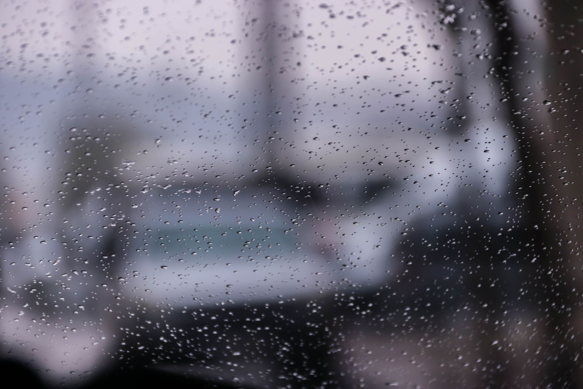 Rain on a glass window with a blurred view of a city and cars in the background, creating a moody atmosphere.