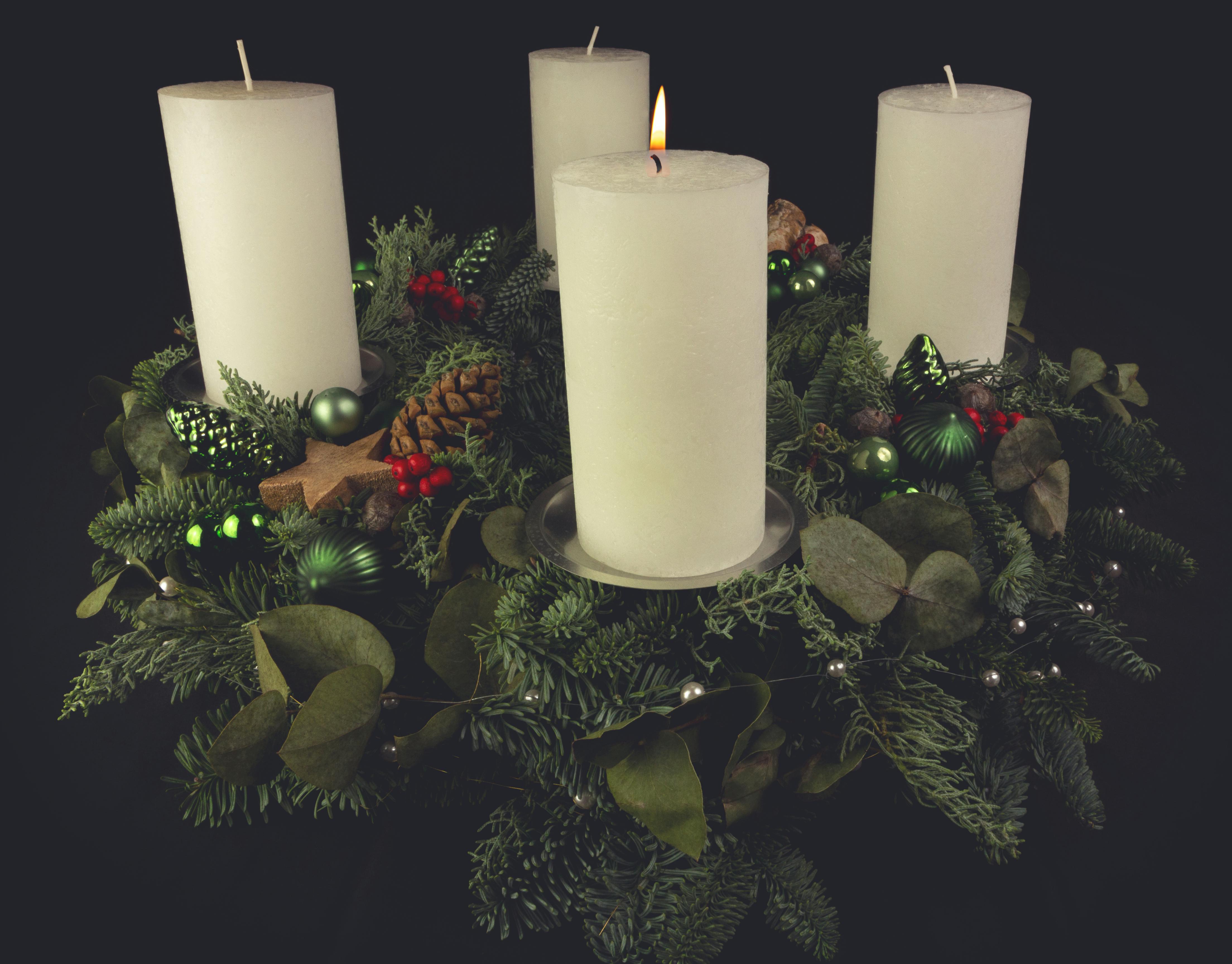 Christmas advent wreath with green foliage, decorated with candles, pinecones, and ornaments.
