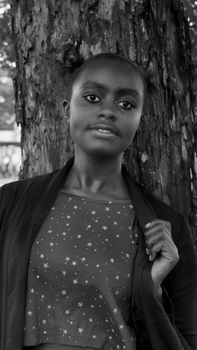 Portrait of a young African woman posing confidently against a tree in a black and white photograph.