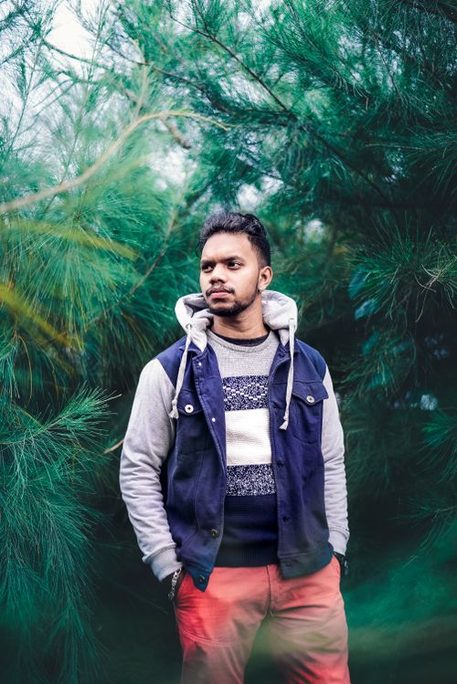 Free Man in hoodie posing among lush green trees, exuding a thoughtful vibe. Stock Photo