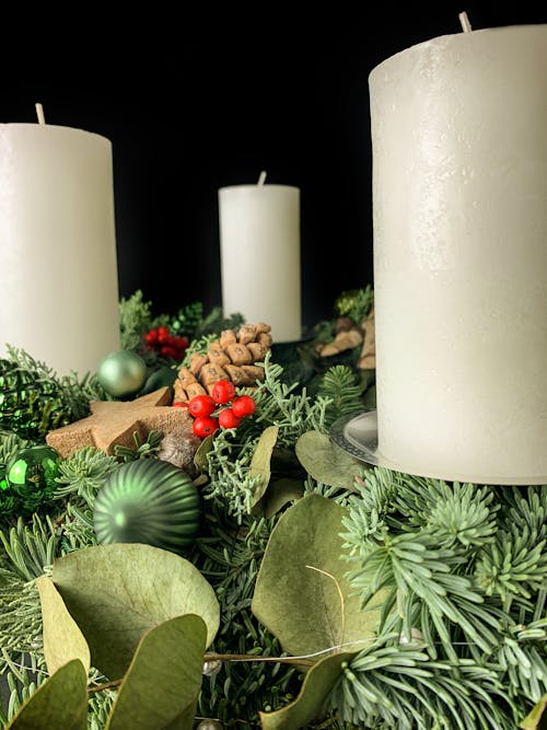 Christmas composition with light candles placed on decorative spruce branches with bumps and baubles against black background