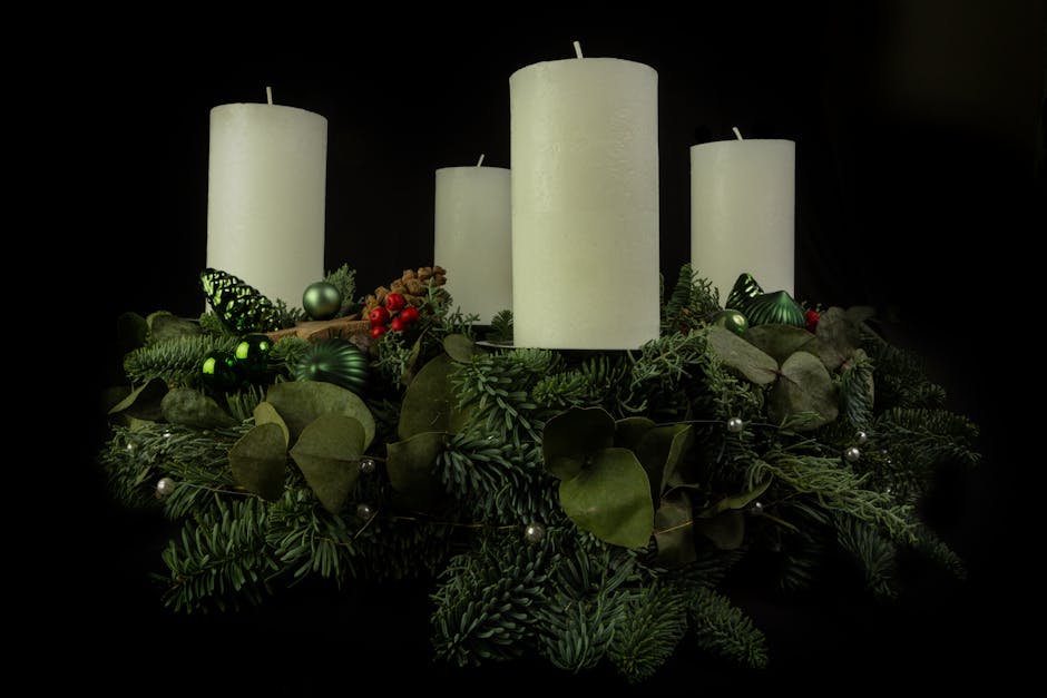 Christmas composition of white candles placed on spruce twigs with baubles against black background in studio