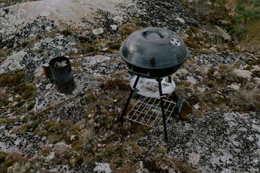 A metal grill and chimney starter on mossy rocks outdoors, perfect for camping BBQ.