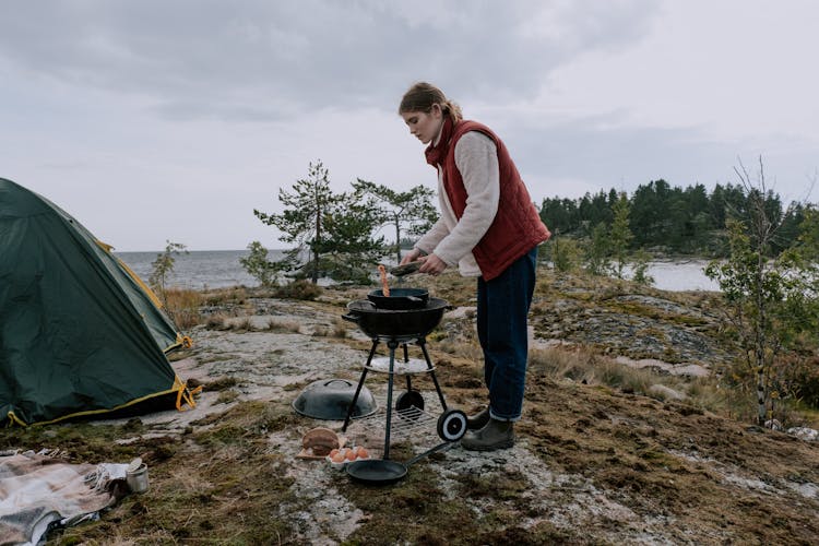 A Woman Cooking On A Charcoal Grill Near The Tent