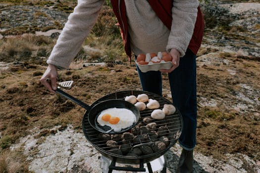 Person cooking eggs on a grill outdoors with mushrooms on a pleasant day.