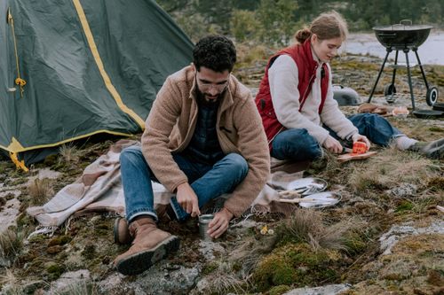 Free Couple enjoying a camping trip, preparing food next to their tent outdoors. Stock Photo
