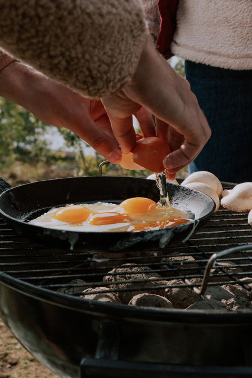 Free Close-up of hands cracking eggs into a frying pan on an outdoor grill. Stock Photo