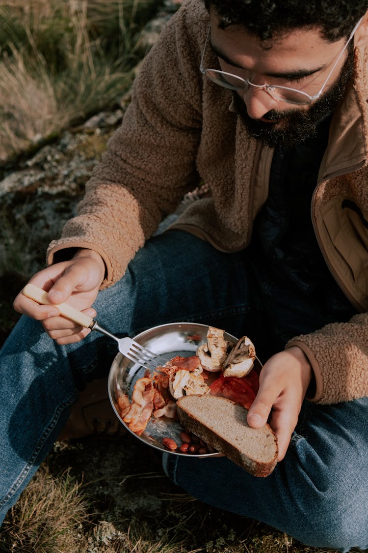 A Bearded Man In Brown Coat Eating Food