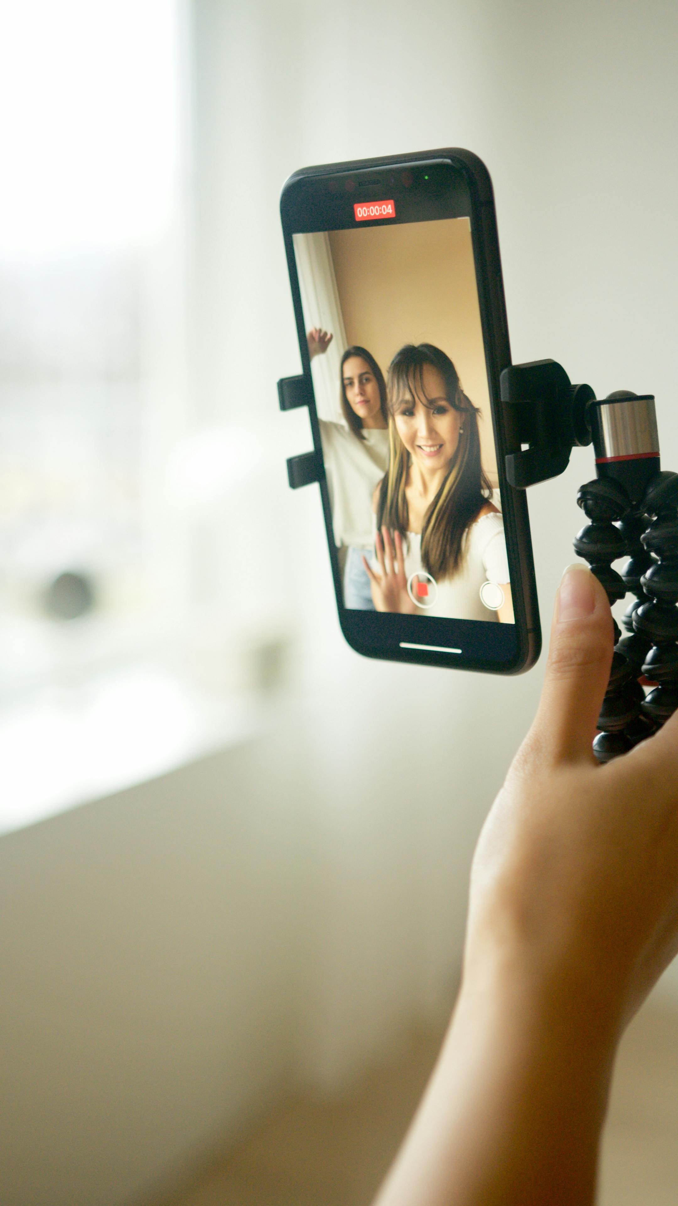 person holding black smartphone taking picture of woman in white shirt