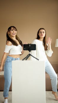 Two young women enjoying a dance session indoors, capturing the moment on a smartphone.