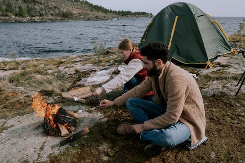 Couple Sitting on Ground Beside Bonfire with Marshmallows