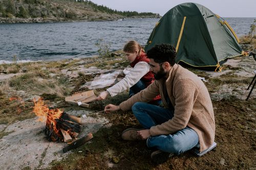 Free Couple enjoying a peaceful camping trip by a lake, roasting marshmallows by a campfire. Stock Photo