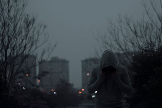 Person in gray hoodie in a dimly lit urban environment with a moody ambiance.