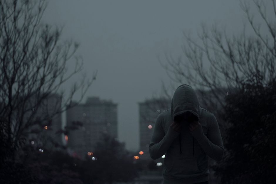 Person in gray hoodie in a dimly lit urban environment with a moody ambiance.