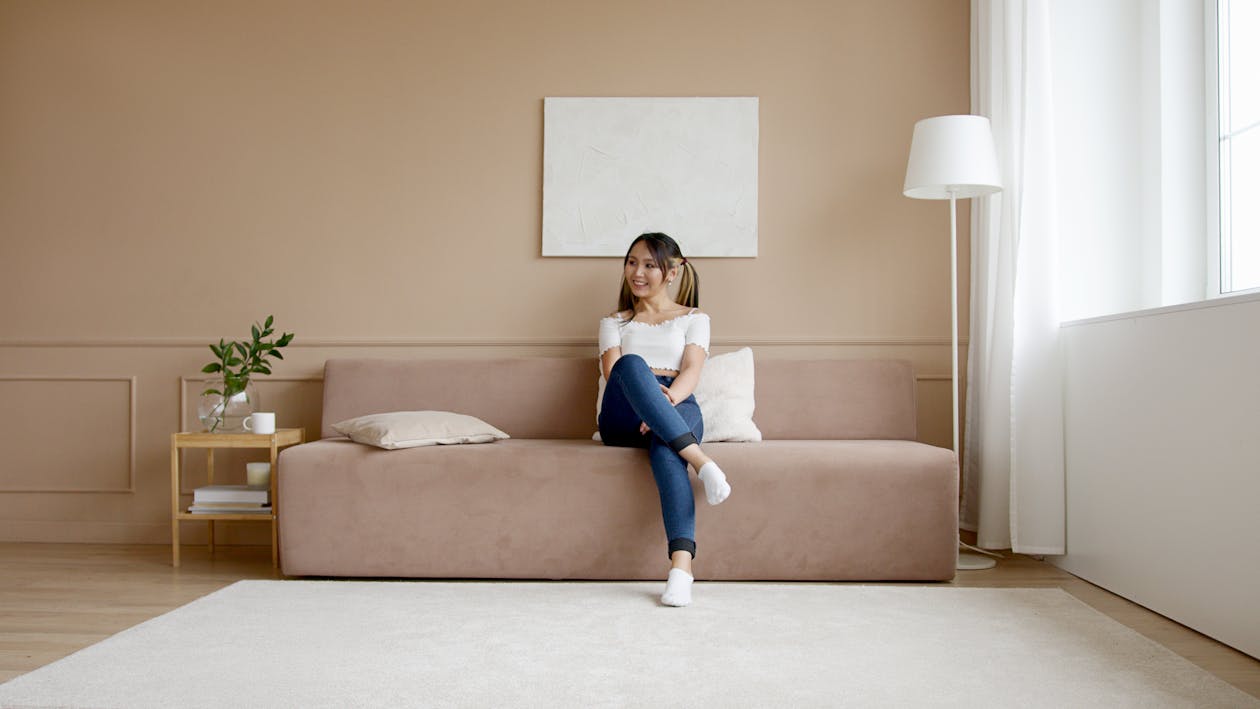 Woman in White T-shirt and Blue Denim Jeans Sitting on Brown Couch